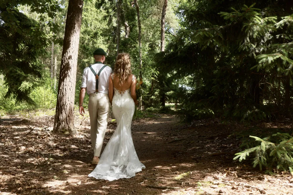 Bruid Linsey Gerrits de Klijn wandelt samen met haar bruidegom door het bos, bruid draagt een elegante kanten trouwjurk met open rug van Bruidshuis Diana.