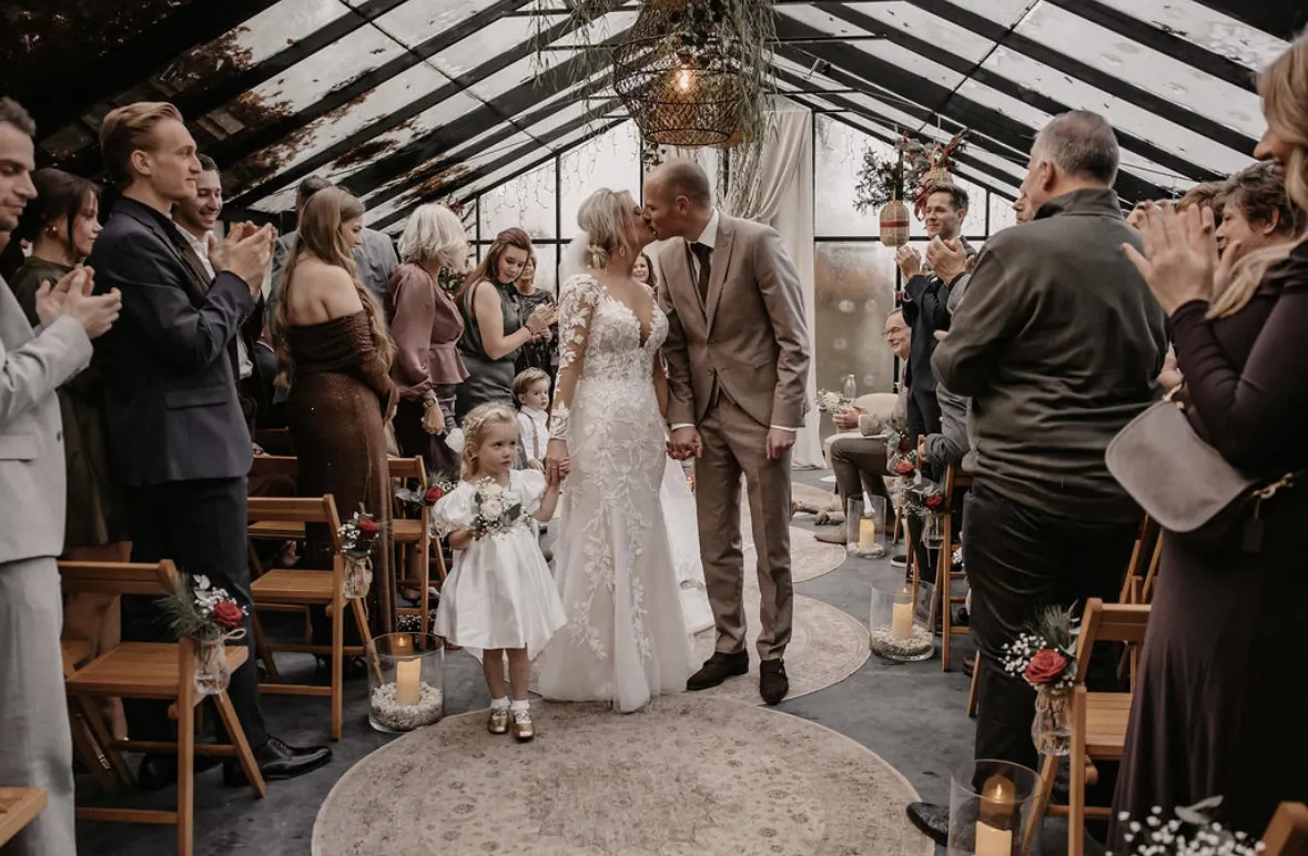real-bride-review-celine-altena-eijsermans-bruidshuis-diana – bruid Celine Altena-Eijsermans en haar bruidegom lopen hand in hand door het gangpad terwijl gasten applaudisseren