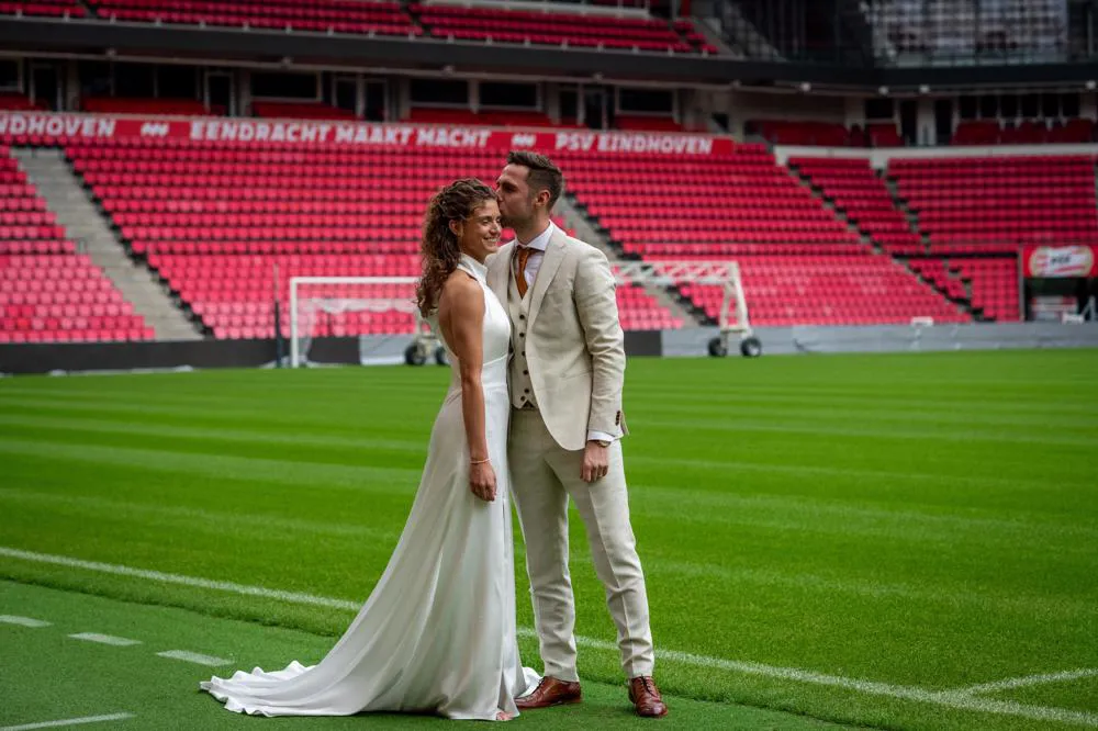 real bride robin verbeek in een elegante fit and flare trouwjurk samen met haar bruidegom op het veld van het psv stadion