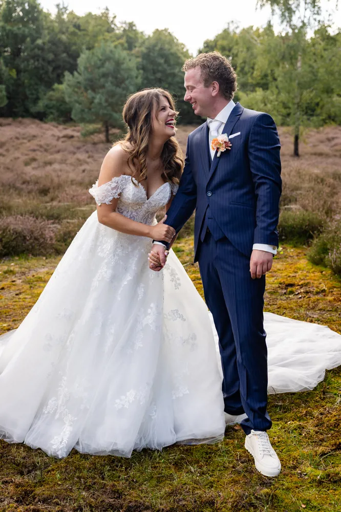 Bruid Birgit Arts deelt een kus met haar bruidegom bij een landelijke trouwlocatie, zij draagt een romantische kanten trouwjurk van Bruidshuis Diana.