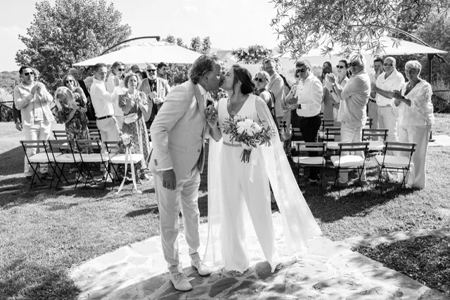 real-bride-review-daphne-de-laat-bruidshuis-diana – bruid Daphne de Laat in een elegante ivoorkleurige jumpsuit met cape mouwen loopt hand in hand met haar bruidegom een stenen trap af tijdens hun bruiloft
